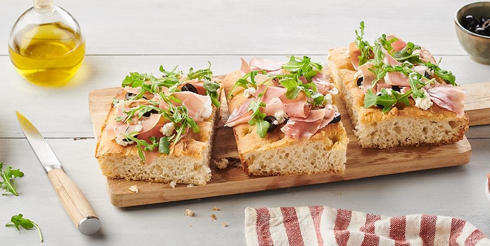 Focaccia au chèvre, jambon cru, roquette et olives noires